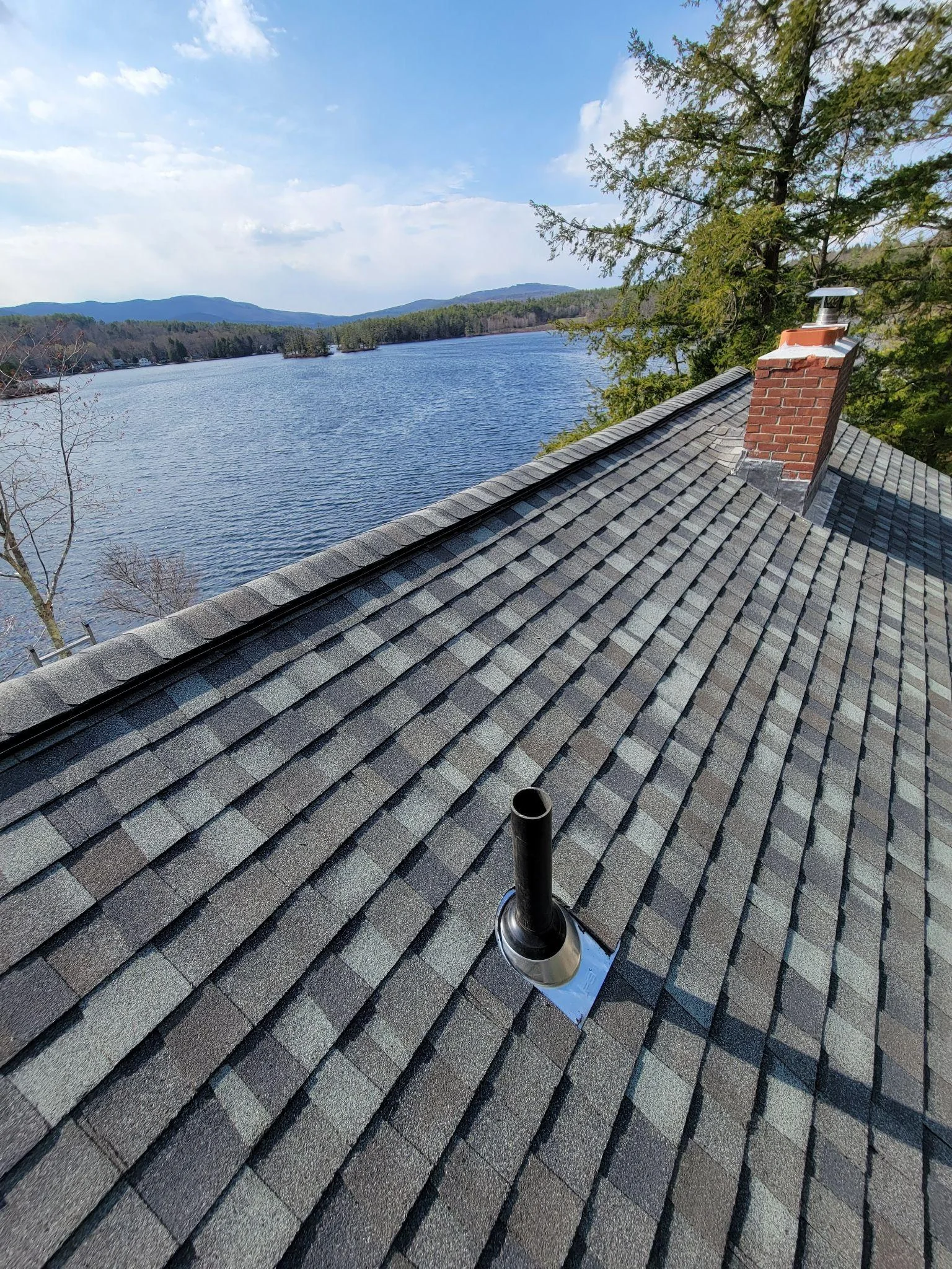 Completed residential asphalt shingle roof replacement overlooking a New Hampshire lake